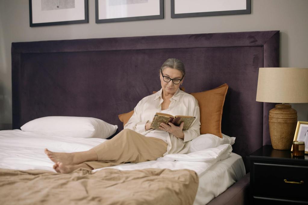 elderly woman sitting on bed while reading a book